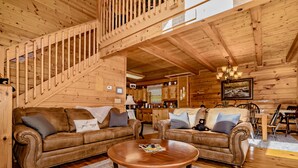 A cozy log cabin interior with two leather sofas, a wooden dining table, and a staircase.