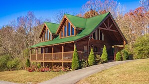 A log cabin with a green roof, a porch, and a stone foundation.