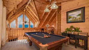 A wooden interior with a pool table, a ceiling fan, and a framed landscape painting.