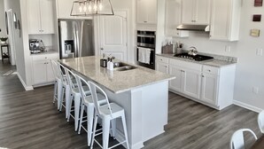 Une cuisine moderne avec des meubles blancs, un grand îlot central doté de tabourets, des appareils en acier inoxydable et un luminaire suspendu.