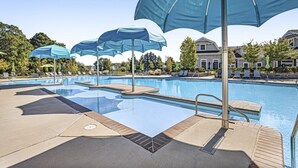 Une piscine bordée de plusieurs parasols bleus, de chaises longues et sous un ciel dégagé.