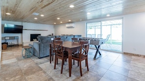 A spacious living area with a wooden ceiling, a sofa set, a dining table with chairs, a foosball table, and a TV mounted on the wall. - Play on the putting green, and enjoy quality time at this amazing home (Scottsdale)