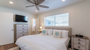 A bedroom with a bed, a ceiling fan, a TV, a dresser, a bedside table, and a window with blinds. - Play on the putting green, and enjoy quality time at this amazing home (Scottsdale)