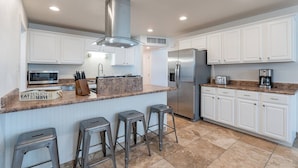 A modern kitchen with white cabinets, a stainless steel refrigerator, a microwave, and a coffee maker. There are three bar stools and a granite countertop. - Play on the putting green, and enjoy quality time at this amazing home (Scottsdale)