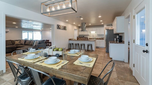 A modern kitchen with white cabinets, a central island, and a dining area with a wooden table set for four. - Play on the putting green, and enjoy quality time at this amazing home (Scottsdale)