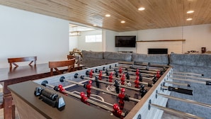 A room with a foosball table, a sofa, a TV, and a dining area. - Play on the putting green, and enjoy quality time at this amazing home (Scottsdale)