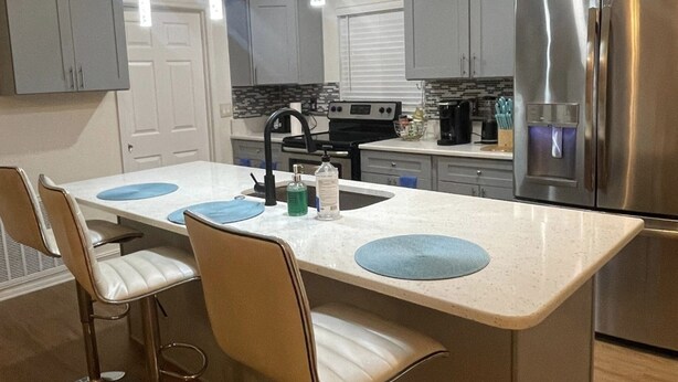 A modern kitchen with a central island, bar stools, stainless steel appliances, and pendant lighting.