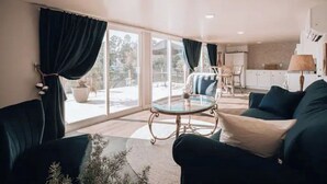 A modern living room with a glass coffee table, dark green sofas, and large windows with curtains. - Douglas Lake -LakeFRONT home w/ Dock (Dandridge)