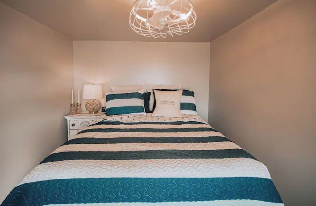 A neatly made bed with striped bedding, a bedside table with a lamp, and a decorative wall hanging.