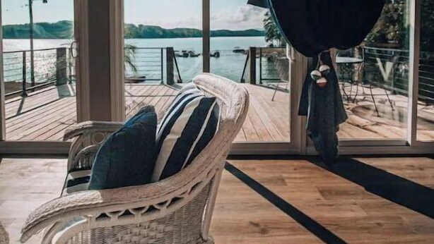 A wicker chair with a striped cushion on a wooden deck, overlooking a body of water with a view of hills in the distance. - Douglas Lake -LakeFRONT home w/ Dock (Dandridge)