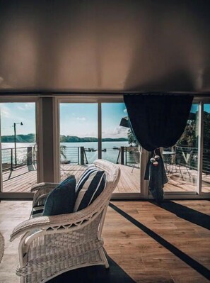 Una silla de mimbre con un cojín a rayas sobre una terraza de madera, con vistas a un cuerpo de agua y colinas a lo lejos.