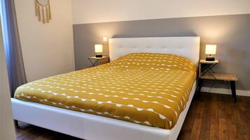 A neatly made bed with a patterned bedspread, two bedside tables with lamps, and a wall-mounted macrame decoration.
