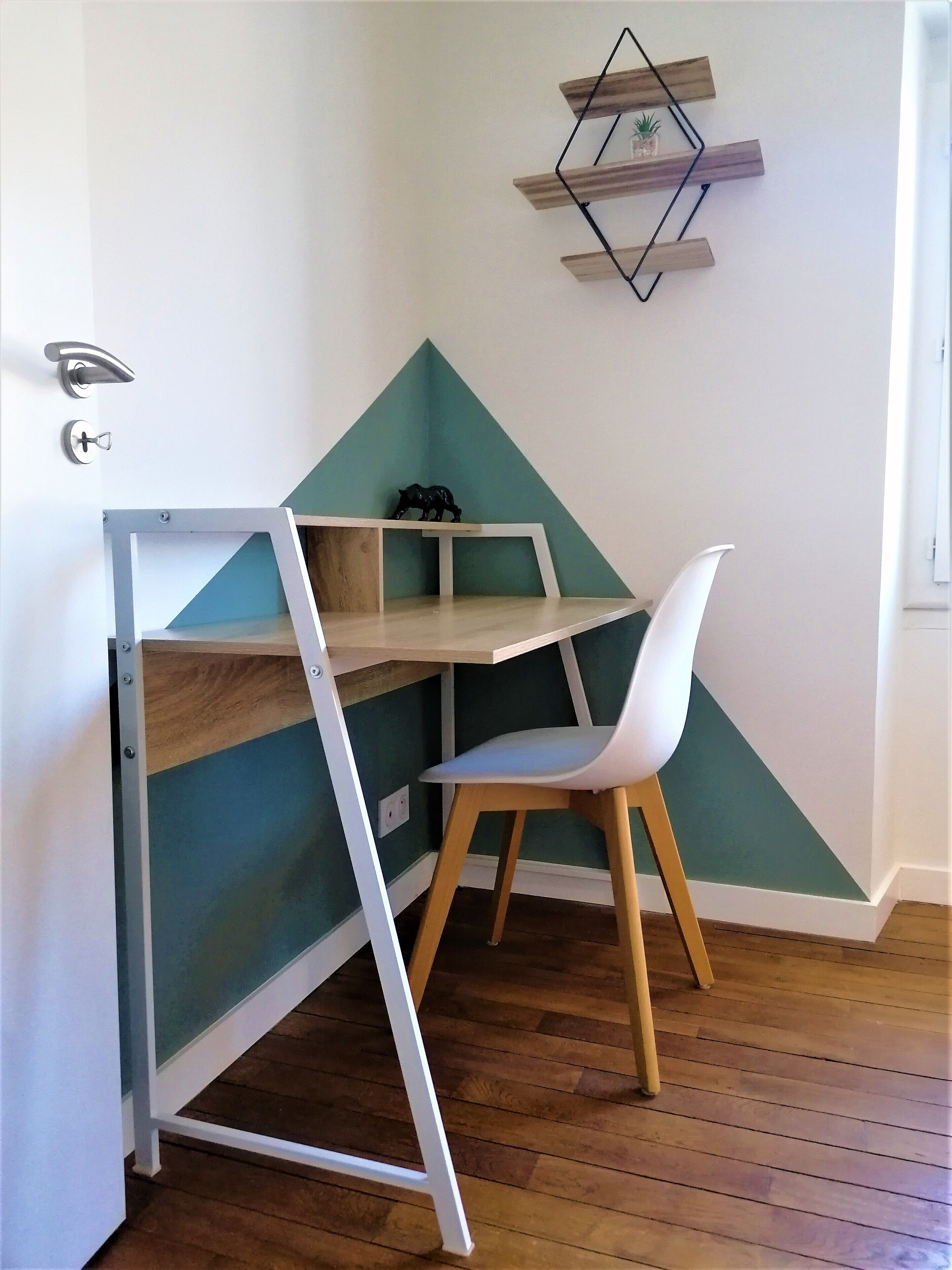 Een hoekbureau met een witte stoel, een wand in teal en een geometrisch decoratieobject aan de muur.