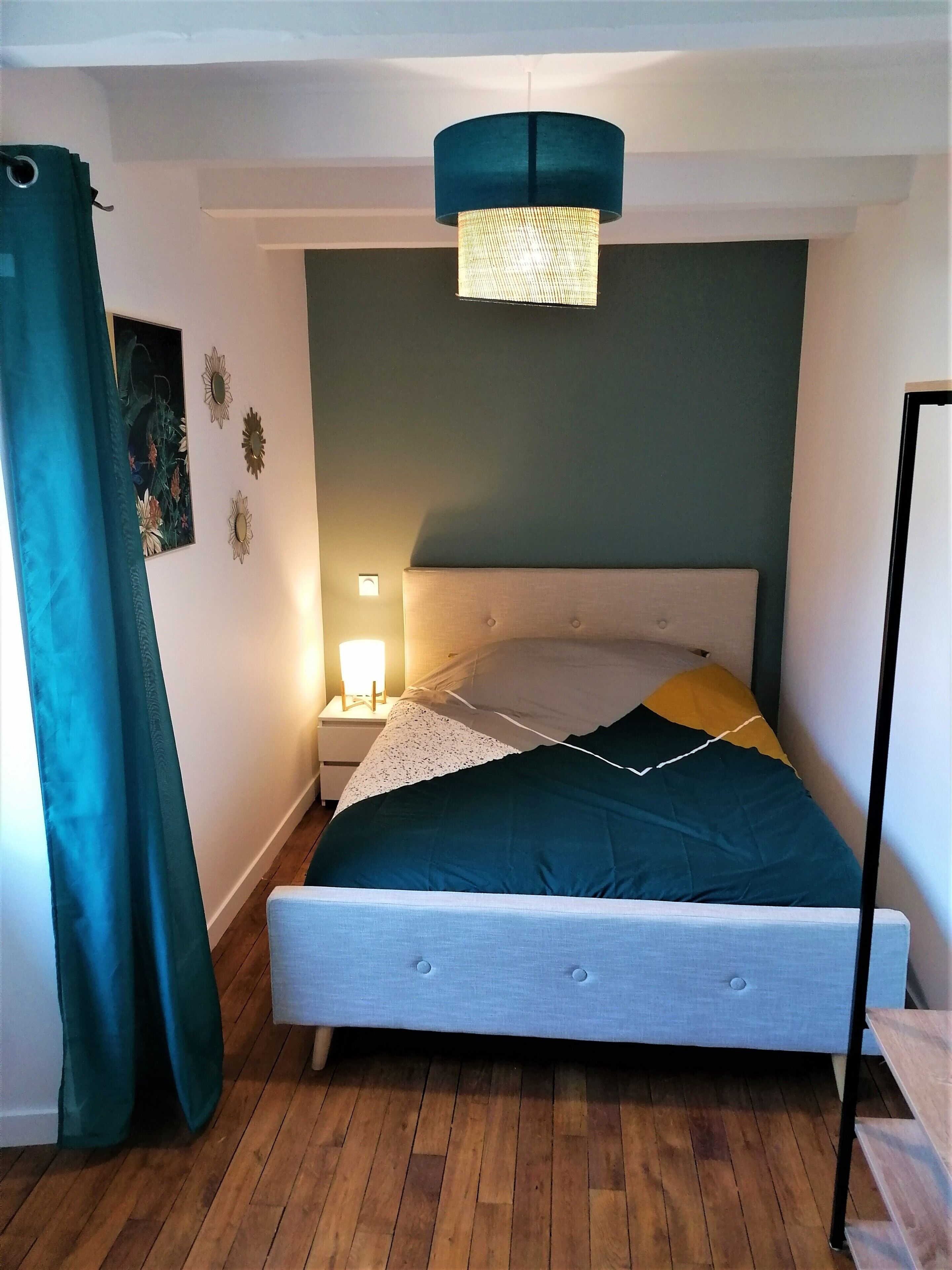 Un dormitorio con cama, mesita de noche, lámpara y cortina.