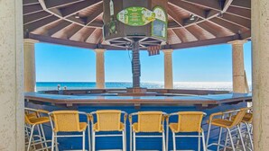 A covered outdoor bar area with a view of the ocean, featuring a central bar with stools and a menu board above.