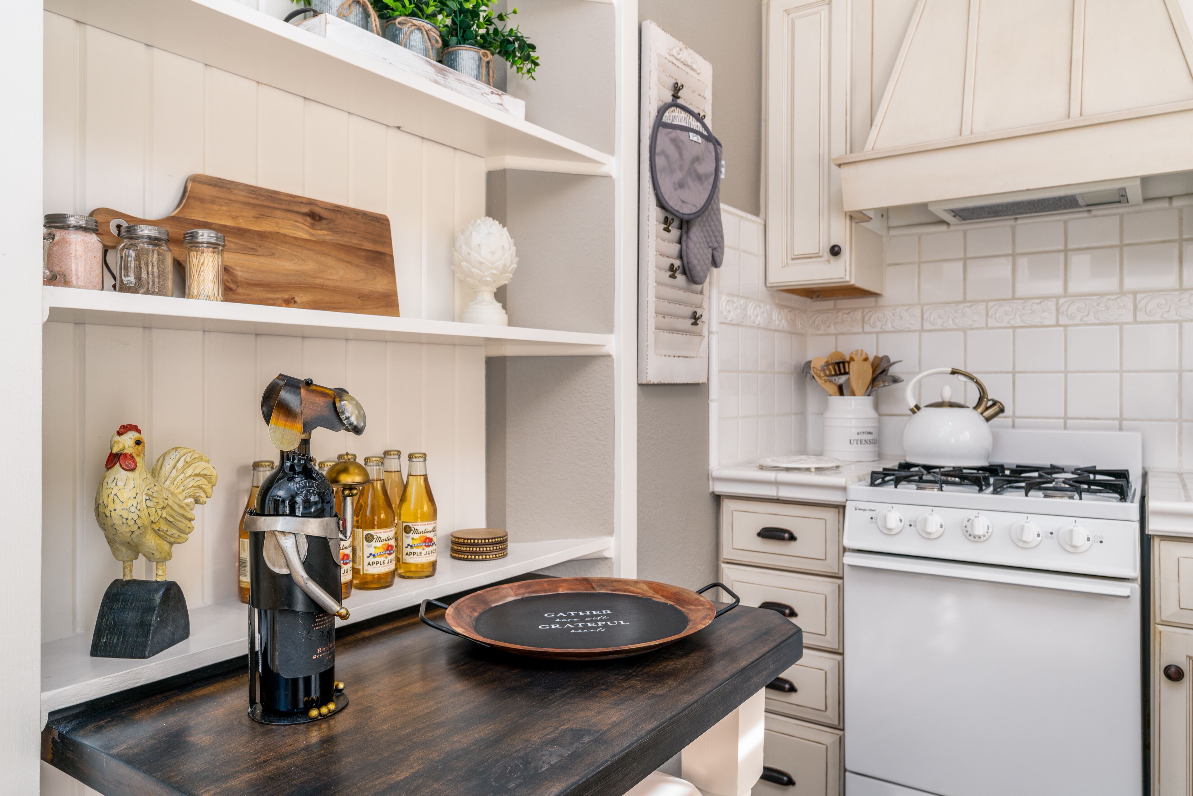 A kitchen with white cabinets, a stove, and a wooden countertop with a coffee press and apple juice bottles.