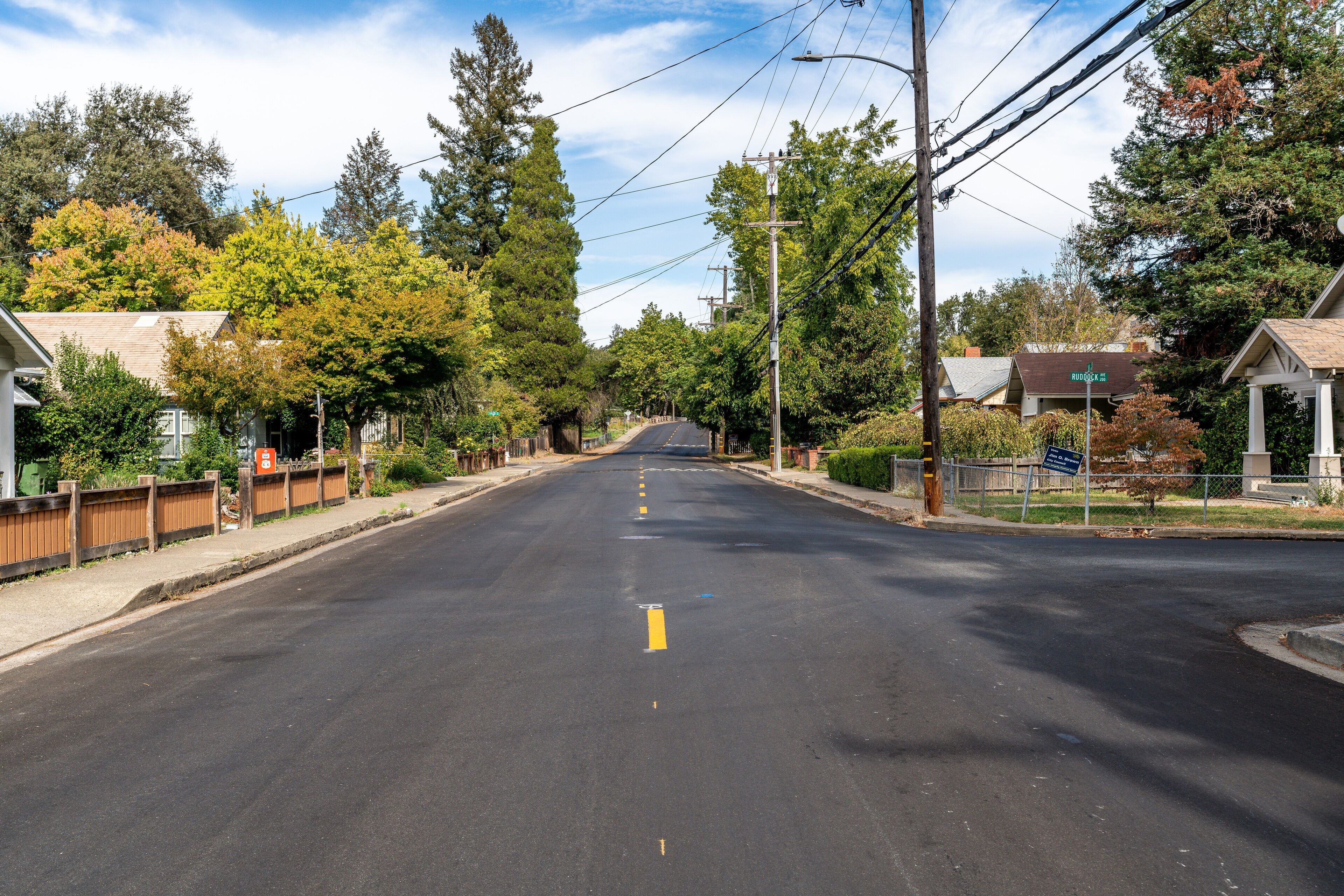 Une rue paisible, située dans un quartier résidentiel, bordée de maisons et d’arbres, où la chaussée est dégagée et les panneaux de signalisation sont bien visibles.