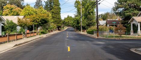 Une rue paisible, située dans un quartier résidentiel, bordée de maisons et d’arbres, où la chaussée est dégagée et les panneaux de signalisation sont bien visibles.
