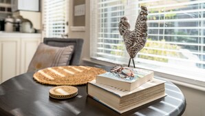 A round table with a woven placemat, a decorative rooster, and a stack of books.