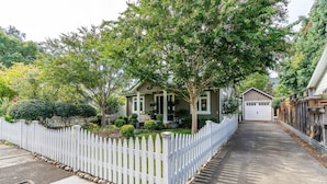 A residential street with a white picket fence, houses, and trees.