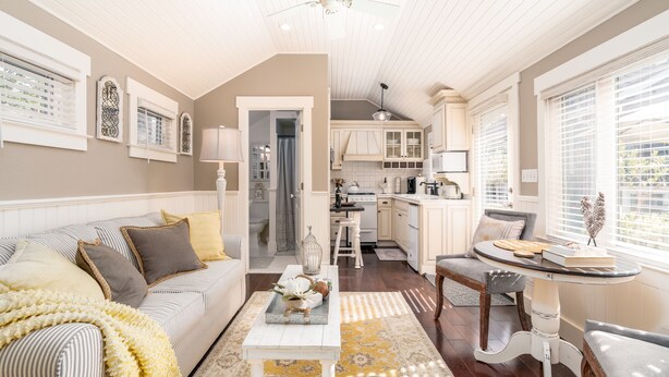 A cozy living room with a sofa, coffee table, and a dining area with a table and chairs. A kitchen is visible in the background.