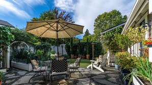 An outdoor patio with a table and chairs, a large umbrella, and various potted plants.