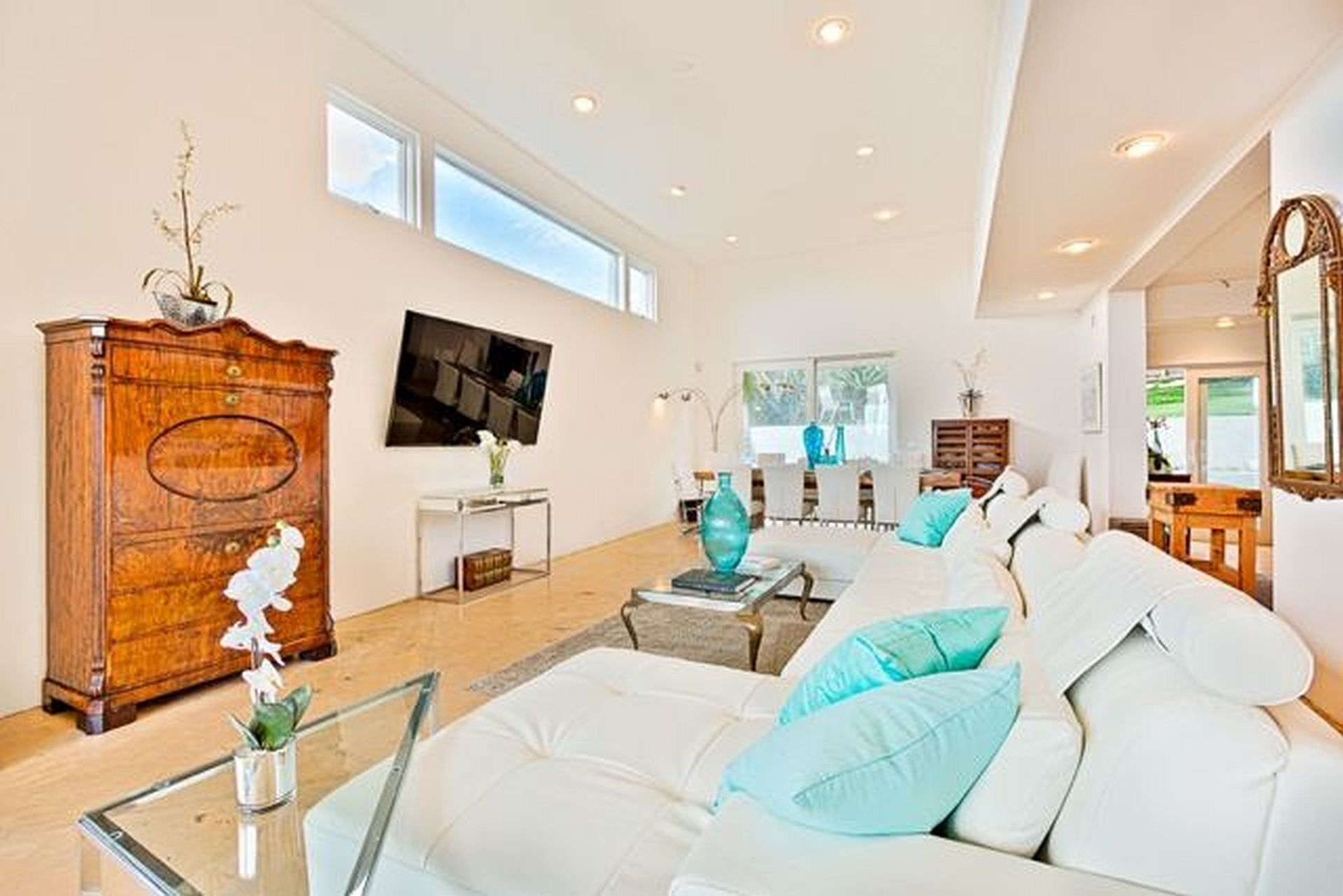 A spacious living room with a white sofa, a wooden cabinet, and a flat-screen TV mounted on the wall.