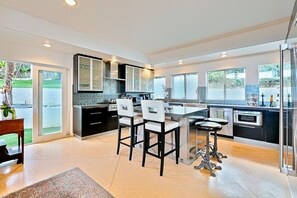 A modern kitchen with a central island, bar stools, and a dining table.