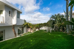 A modern house with a well-maintained lawn, a patio area with chairs, and tropical plants.