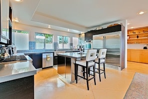 A modern kitchen with a central island, stainless steel appliances, and a seating area with chairs.