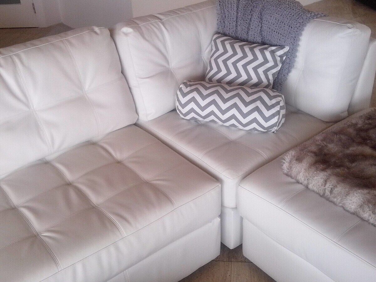 Un sofá de cuero blanco con una manta suave y dos cojines estampados.