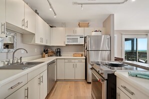 Une cuisine moderne dotée d’appareils électroménagers en acier inoxydable, de meubles blancs et offrant une vue sur l’extérieur.