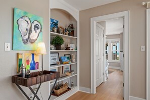 A hallway with a wooden floor, a white door, and a shelf with various decorative items.