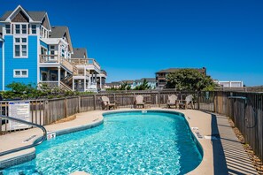 Une piscine dotée d’une terrasse en bois, entourée d’une clôture en bois, et située à côté d’un immeuble à plusieurs étages doté de balcons.