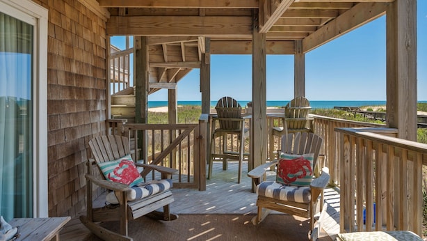 A wooden deck with two Adirondack chairs and a table, overlooking a beach. - Sand Flee: Oceanfront condo, first level, awesome ocean views, community pool (Kill Devil Hills)