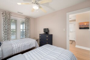 A bedroom with two beds, a dresser, a ceiling fan, and a painting on the wall. - Sand Flee: Oceanfront condo, first level, awesome ocean views, community pool (Kill Devil Hills)