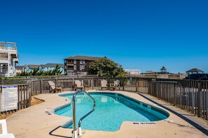 A swimming pool with a wooden deck and lounge chairs, surrounded by a wooden fence and a sign with pool rules. - Sand Flee: Oceanfront condo, first level, awesome ocean views, community pool (Kill Devil Hills)
