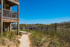 A wooden structure with a balcony, a sandy path leading to it, and a fence in the background.