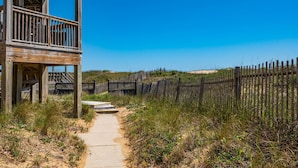 A wooden structure with a balcony, a pathway leading to a sandy beach, and a wooden fence. - Sand Flee: Oceanfront condo, first level, awesome ocean views, community pool (Kill Devil Hills)
