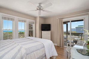 A bedroom with a bed, a television, a balcony with a table and chairs, and a view of the sea.