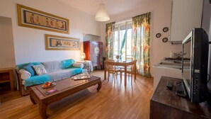 A living room with a sofa, coffee table, and dining area. There is a television on a stand and a clock on the wall. - Penthouse in cit turin (Torino)