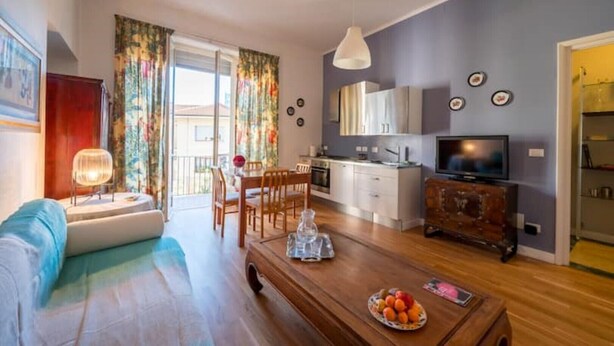 A living room with a sofa, coffee table, and a dining area with chairs. There is a kitchen with cabinets and a TV. - Penthouse in cit turin (Torino)