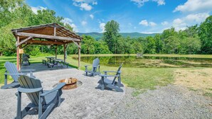 A covered outdoor seating area with Adirondack chairs and a fire pit, overlooking a lake and forested hills. - Mtn Views & Idyllic Setting! Clifton Forge Retreat (Clifton Forge)
