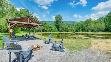 Un espace extérieur aménagé, abrité et doté de chaises Adirondack et d’un foyer, offrant une vue sur un lac et des collines boisées.
