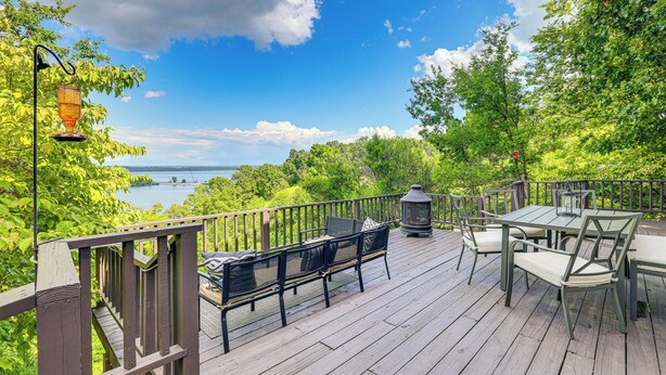 Eine Holzterrasse mit Gartenmöbeln, einer Laterne und Blick auf das Wasser.