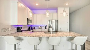 Una cucina moderna con mobili bianchi, un piano di lavoro in granito, elettrodomestici in acciaio inossidabile e illuminazione a sospensione.