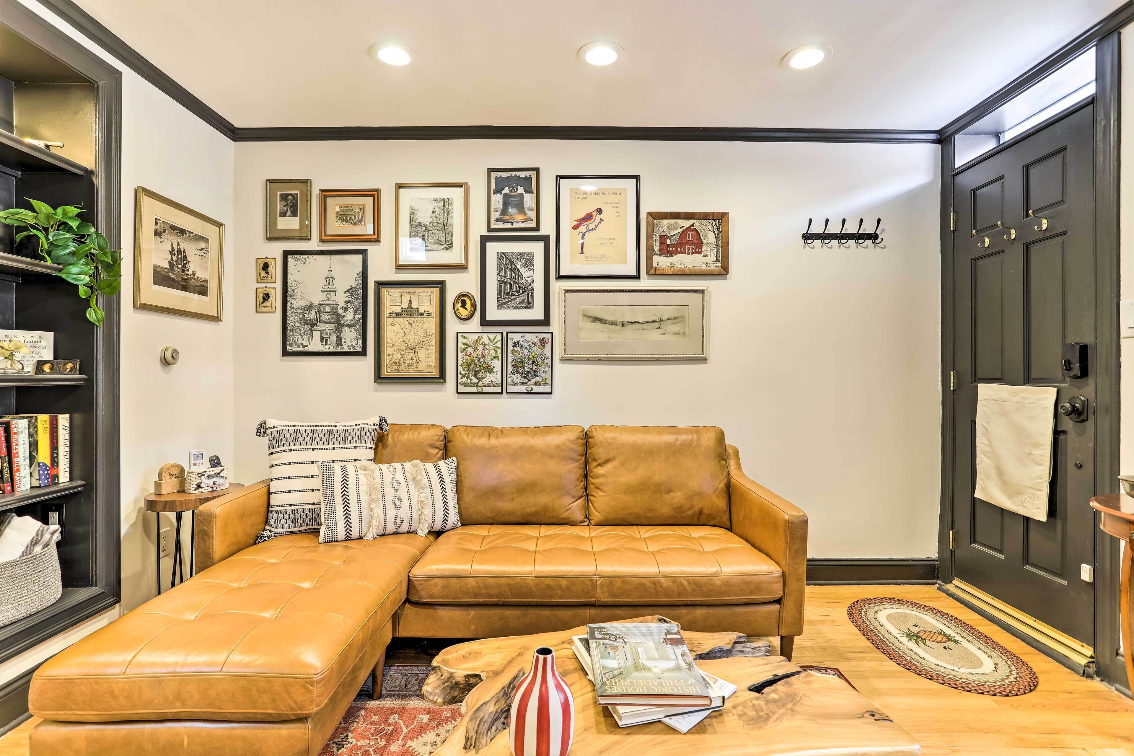 Una sala de estar con un sofá de cuero marrón, una mesa de centro con libros y una pared decorada con obras de arte enmarcadas.