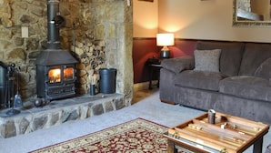 Un salon chaleureux avec une cheminée en pierre, un canapé, une table basse en bois et un tapis à motifs.
