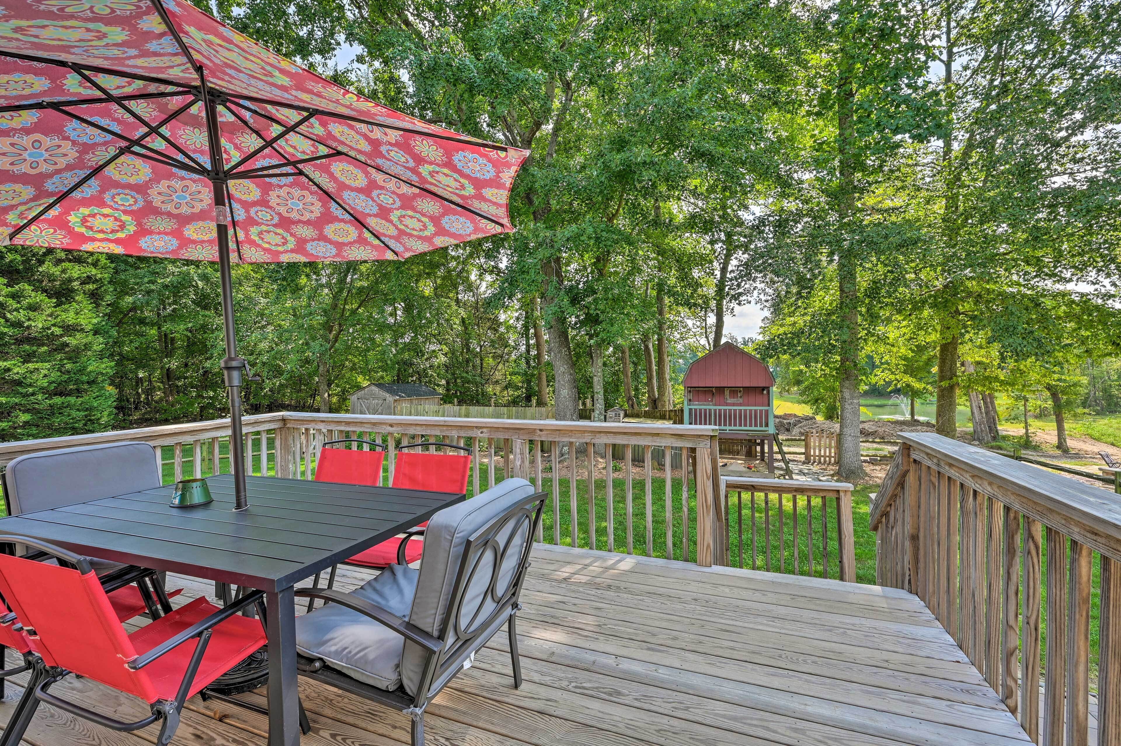 A deck with a table and chairs, a red umbrella, and a wooden deck railing.