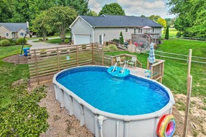 An above-ground swimming pool with a wooden deck, surrounded by a fenced yard and a house in the background. - Peaceful Country Retreat w/ Easy Highway Access! (Browns Summit)